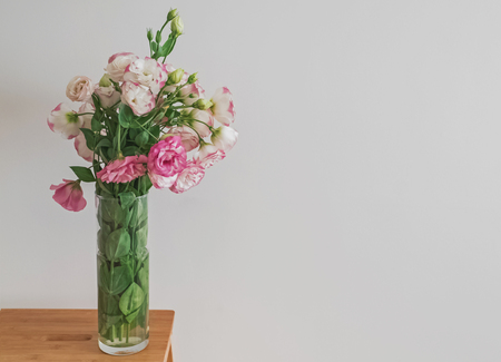 Pink flowers in a glass vase standing near the white wallの写真素材