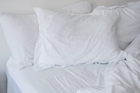 Unmade bed close-up with white bedsheet and pillows.の写真素材