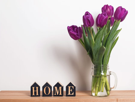 Purple tulips in a glass jar standing near thewall in the living room