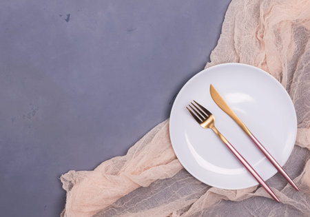 Empty white plate and modern design cutlery on the gray stone table