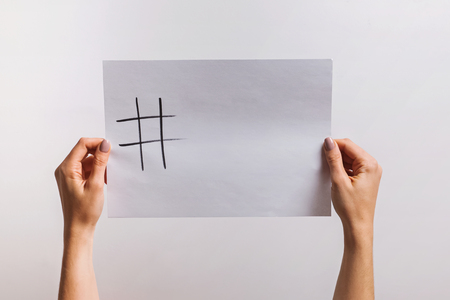 Womans hands holding a paper with drawn hashtag symbol and some copy space on itの写真素材