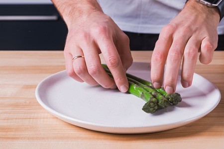 Close-up shot of mans hands laying out steamed green asparagus on the plate,の写真素材