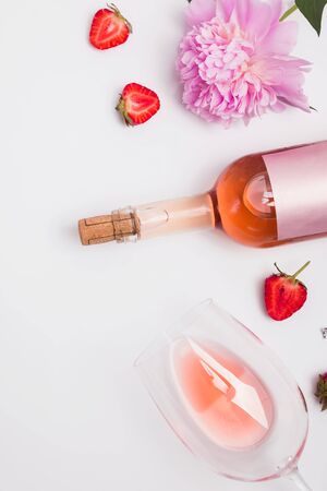 Creative summer flat lay with rose wine, delicious strawberries and beautiful peonies on the white backgroundの写真素材