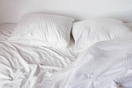 Messy bed with white pillows and sheetsの写真素材