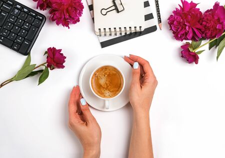 Womans hands holding a cup of coffee on the table with feminine accessories and peonies.の写真素材