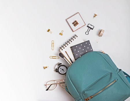 Student's backpack with different stationery and study supplies on the white background, top view....