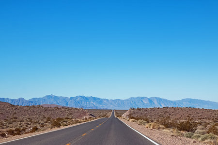 Empty asphalt road through the desert in a sunny day with mountains on the background