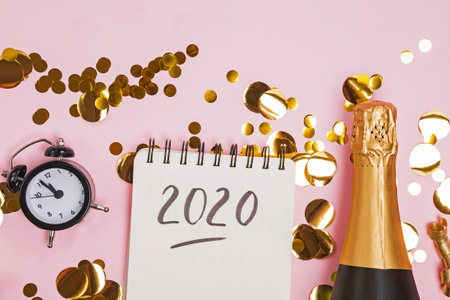 Creative composition with clock, golden confetti and notepad with text 2020.
