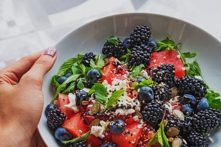 Womans hand holding a plate with delicious salad with watermelon, arugula and berriesの写真素材