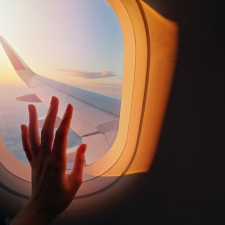 Womans hand touching a window glass on the plane in sunset light