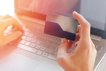Man holding a plastic credit card near the computer close-up.