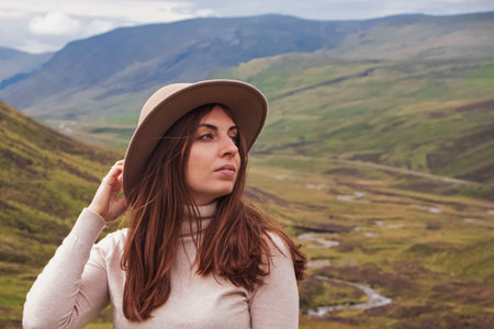 Woman traveller in mountains wearing beige sweater and hat looking in the distance