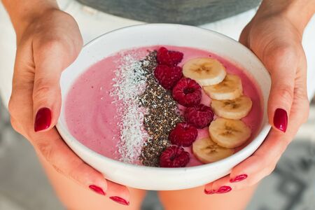 Womans hands holding smoothie bowl with raspberries and bananas close-up.の写真素材