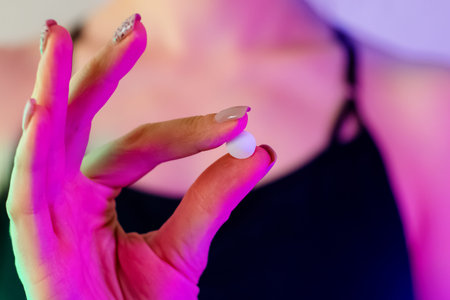Womans hand close-up holding drug pill in neon light
