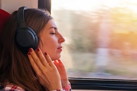Woman enjoying music in her headphones sitting near the windowの写真素材