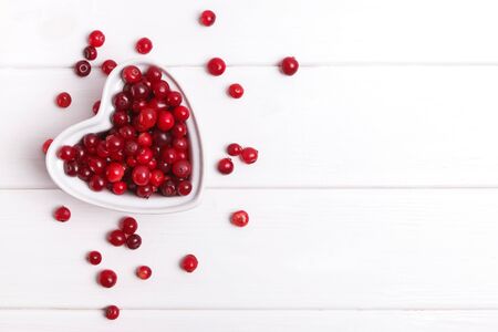 Fresh cranberry berries in a heart shaped bowl on white wooden tableの写真素材