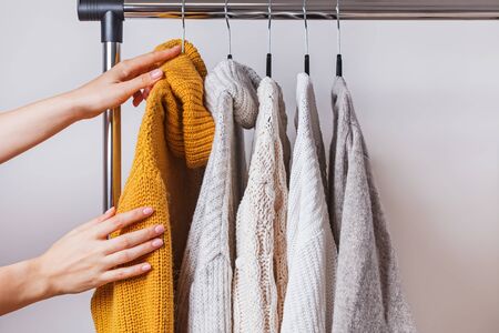 Womans hands choosing yellow knitted sweater among others on hangerの写真素材