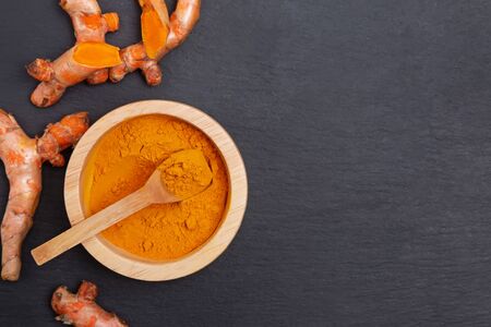 Turmeric powder and roots on the black stone backgroundの写真素材