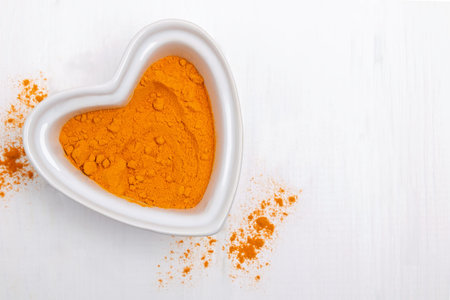 Bright yellow powder spice, turmeric or curry in a heart shaped bowl on the white tableの写真素材