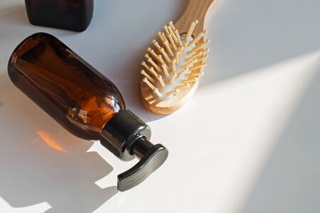 Shampoo in glass bottle and wooden hair brush on the table with dropping shadows.の写真素材