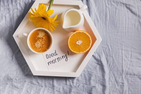 Tray with coffee, milk, orange and yellow flower on it standing on the bedの写真素材