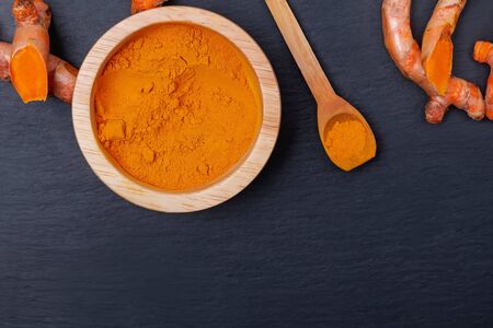 Turmeric powder in wooden bowl and roots on black stone background,の写真素材