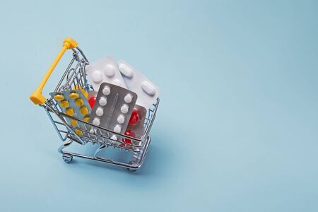 Miniature shopping trolley full of pills on pastel light blue background.の写真素材