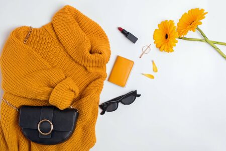 Stylish female clothes and accessories set, top view. Woman outfit with yellow sweater, bag, sunglasses and two gerbera flowers on white background.の写真素材