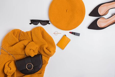 Stylish female clothes and accessories set, top view. Woman outfit with yellow sweater, french beret, hand bag, sunglasses and other items on white backgroundの写真素材