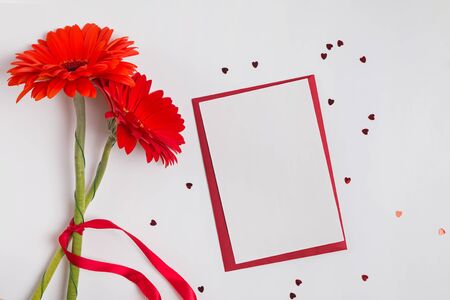Blank card and red gerbera flowers on white background with small heart shaped confetti. Festive background, Valentine's day mock-up.の写真素材