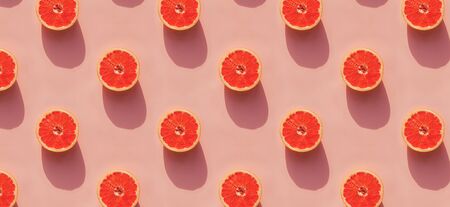 Grapefruit halves on pink background with natural light shadows.の写真素材