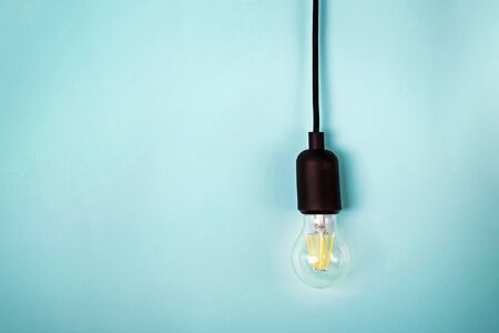 Retro electric light bulb with cord isolated on turquoise color background with copy space.の写真素材