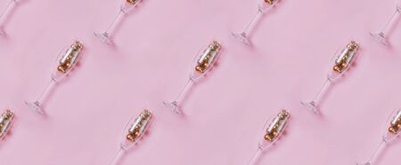 Champagne glasses with golden and red baubles inside on pastel pink backgroundの写真素材