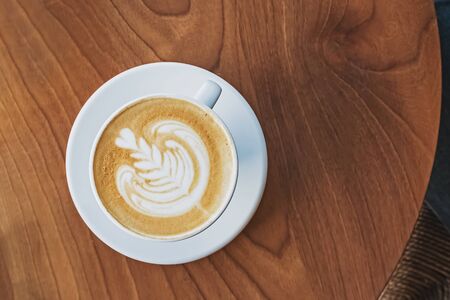 A cup of coffee with latte art on the wooden table, top viewの写真素材