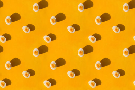 Boiled eggs cut in half on yellow background, flat lay. Creative pattern.