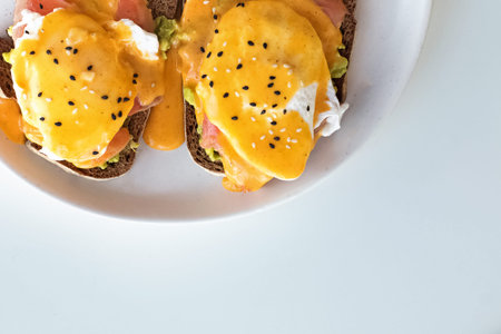 Toasts with avocado, salmon, poached egg and hollandaise sauce on a white plate.
