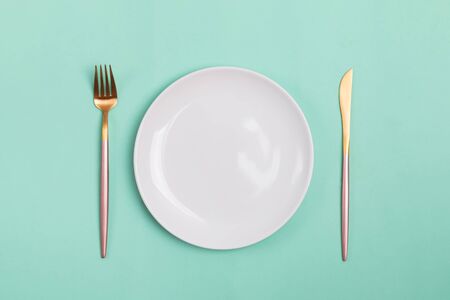 Modern design knife, fork and white plate on pastel green backgroundの写真素材