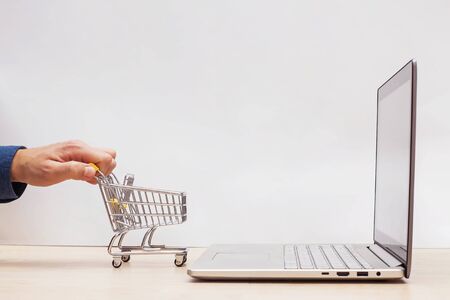 Hand holding mini shopping trolley near the opened laptop on yellow background.の写真素材