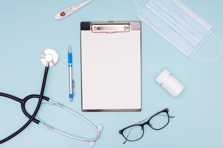 Medical mock-up with blank sheet of paper on the clipboard, and stethoscope, medical mask and other...