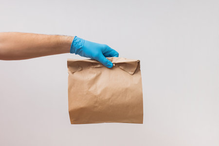 Courier wearing protective gloves and mask holding paper bag with food