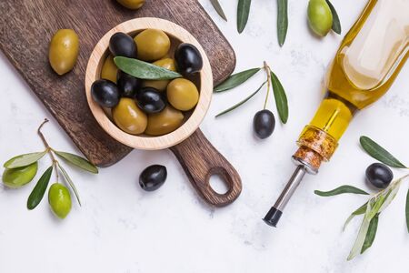 Black and green olives in wooden bowl and bottle of oil on white marble table,の写真素材