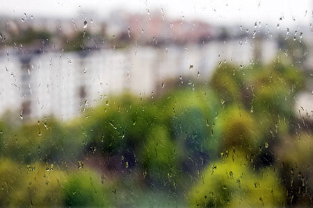 Close-up shot of rain drops on the window with blurred spring city landscape at the background