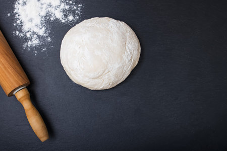 Dough, rolling pin and flour on a black background