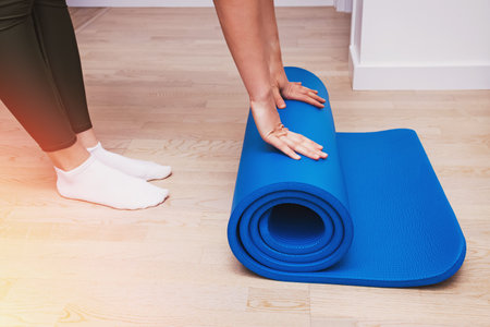 Close-up of woman folding blue yoga or fitness mat after working out at homeの写真素材