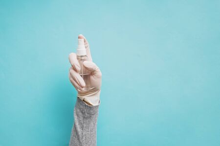 Womans hand in medical protective glove hand holding sanitizer spay bottle on blue backgroundの写真素材
