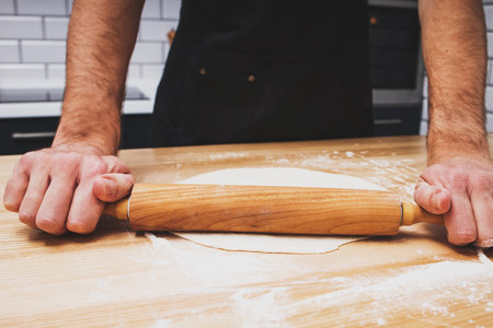 Close up shot of man's hands rolling dough on wooden table