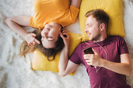 Top view of beautiful young loving couple lying and sharing headphonesの写真素材