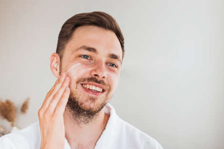 Handsome young man applying cream on his faceの写真素材