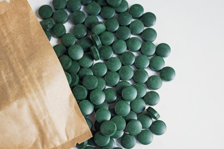 Green pills on wooden scoop isolated on white background with reflection. Spirulina, chlorella and...