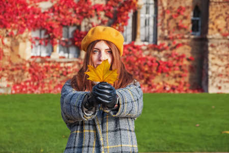 Young beautiful woman in yellow beret holding maple leaf.の写真素材
